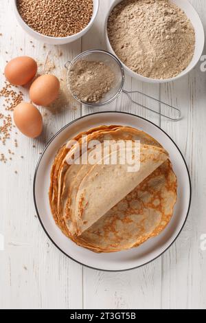 Traditionnel français salé sarrasin galettes Bretonnes crêpes sur une table avec de la farine, des céréales et des œufs closeup sur la table en bois blanc. Haut vertical Banque D'Images