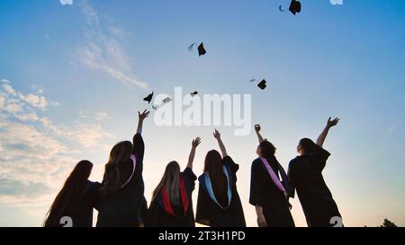 Les silhouettes des diplômés jettent leurs casquettes au coucher du soleil. Banque D'Images