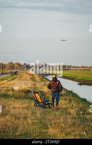 Un homme avec une chaise pliante regarde un 747 atterrir sur le Polderbaan à l'aéroport d'Amsterdam Schiphol, aux pays-Bas. La piste est sécurisée par un canal Banque D'Images