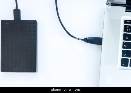 disque dur ssd noir avec câble connecté à un ordinateur portable avec fond blanc Banque D'Images