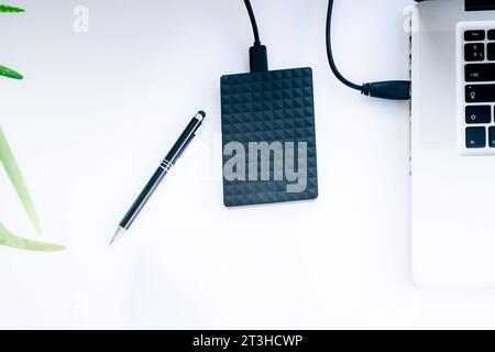 stylo et disque dur ssd noir avec câble connecté à un ordinateur portable avec fond blanc Banque D'Images