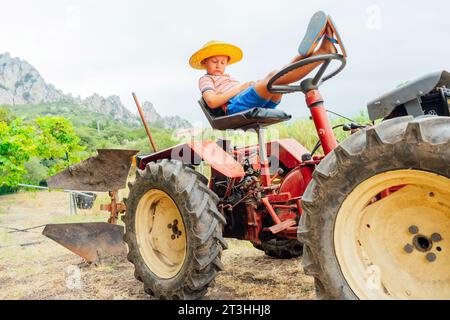 Petit garçon fermier sur un tracteur parmi les champs de céréales vertes Banque D'Images