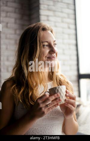 Le visage d'une femme est illuminé par la joie d'un nouveau jour, alors qu'elle sirote son café du matin Banque D'Images