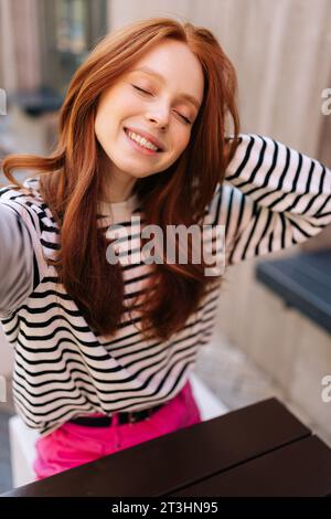 Portrait POV vertical de femme souriante avec les yeux fermés prenant l'autoportrait avec smartphone assis à table dans le café. Le point de vue de la pratique féminine Banque D'Images