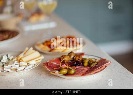Deux verres de champagne frais et des assiettes avec diverses collations sur une table. Assiettes blanches avec tranches de jambon, salami, câpres, olives et fromage. Cozy int Banque D'Images
