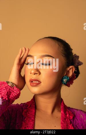 Portrait de femme balinaise avec robe rose pose avec les mains sur le visage à l'intérieur de la pièce Banque D'Images