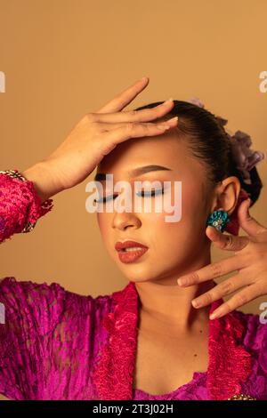 Portrait de femme balinaise avec robe rose pose avec les mains sur le visage à l'intérieur de la pièce Banque D'Images