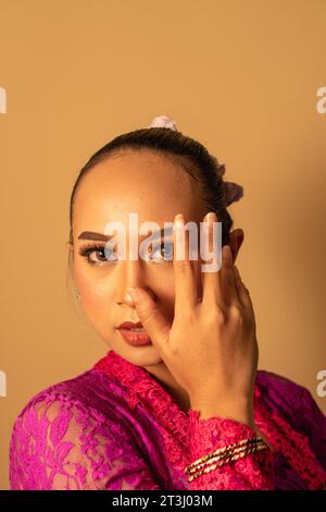 Portrait de femme balinaise avec robe rose pose avec les mains sur le visage à l'intérieur de la pièce Banque D'Images