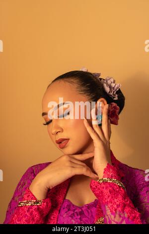 Portrait de femme balinaise avec robe rose pose avec les mains sur le visage à l'intérieur de la pièce Banque D'Images