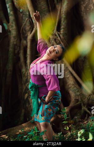 Femme asiatique prend une pose de danse dans la jungle tout en portant une robe violette et un collier d'or avec un beau sourire sur son visage Banque D'Images