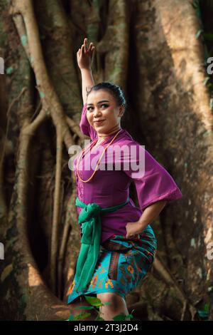 Femme asiatique prend une pose de danse dans la jungle tout en portant une robe violette et un collier d'or avec un beau sourire sur son visage Banque D'Images