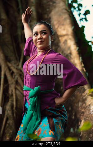 Une femme indonésienne pose courageusement en levant les mains dans une robe violette tout en se tenant debout dans la forêt Banque D'Images