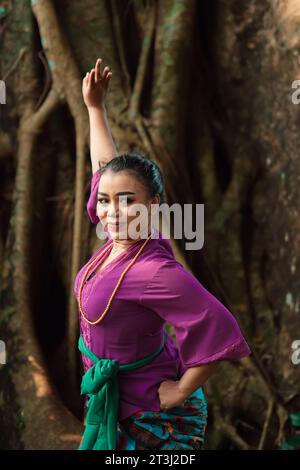 Une femme indonésienne pose courageusement en levant les mains dans une robe violette tout en se tenant debout dans la forêt Banque D'Images