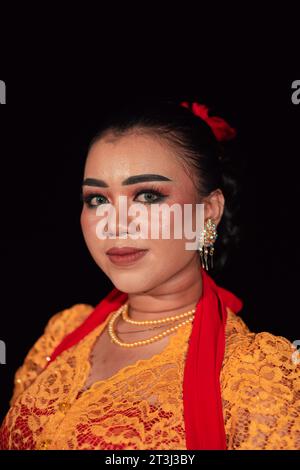 Femme javanaise dans une robe orange traditionnelle tout en portant le maquillage et une écharpe rouge à un festival de danse en Indonésie Banque D'Images