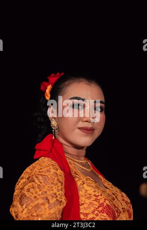 Femme javanaise dans une robe orange traditionnelle tout en portant le maquillage et une écharpe rouge à un festival de danse en Indonésie Banque D'Images