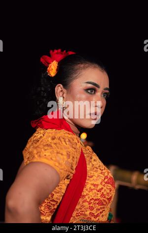 Femme javanaise dans une robe orange traditionnelle tout en portant le maquillage et une écharpe rouge à un festival de danse en Indonésie Banque D'Images