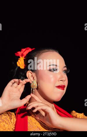 Femme javanaise exotique portant un beau maquillage avec des lèvres rouges tout en portant un costume jaune traditionnel et une écharpe rouge à l'intérieur du village Banque D'Images