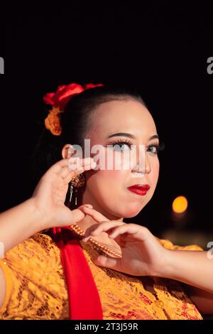 Femme javanaise exotique portant un beau maquillage avec des lèvres rouges tout en portant un costume jaune traditionnel et une écharpe rouge à l'intérieur du village Banque D'Images