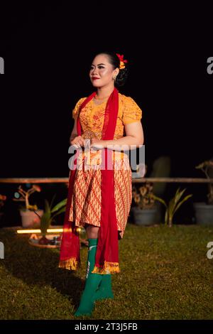 Mignonne femme indonésienne avec des lèvres rouges et une écharpe rouge portant une robe traditionnelle sundanaise appelée kebaya à l'intérieur du festival de danse Banque D'Images