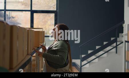 Chef de la logistique en entrepôt gérant des boîtes en carton pleines de produits prêts à être expédiés aux clients. Superviseur méticuleux dans le centre de distribution plaçant les colis sur les étagères de l'armoire Banque D'Images