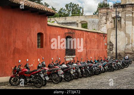 Guatemala, la Antigua - 20 juillet 2023 : longue rangée de motos de banlieue sur le côté de la rue devant un mur peint en rouge. Ruine de l'église de la conception en ba Banque D'Images