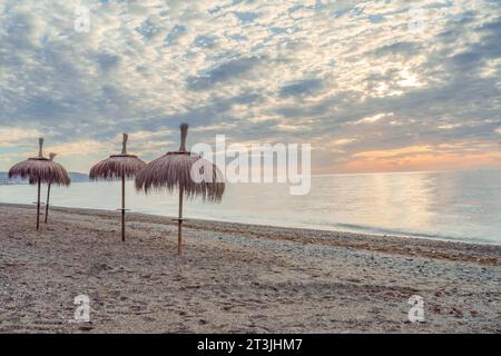 San pedro alcantara, malaga, espagne Paysage de mer avec parasols de chaume à l'aube avec une mer calme Banque D'Images