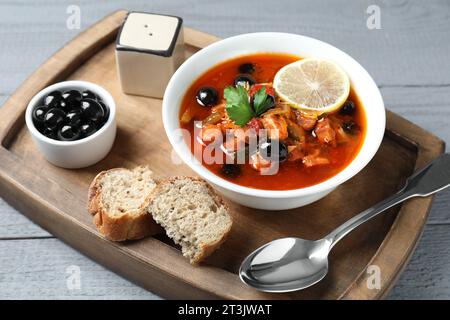 Soupe solyanka à la viande avec saucisses, olives et légumes dans un bol servi sur une table en bois gris Banque D'Images