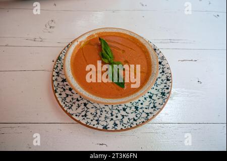 Gazpacho aux couleurs vives orange et vert, servi dans un bol rustique sur une belle assiette bleue au-dessus d'une table blanche patinée. Banque D'Images