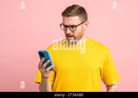 Homme barbu demandé dans des lunettes regardant l'écran de téléphone portable dans la surprise choqué par le message, les nouvelles Banque D'Images