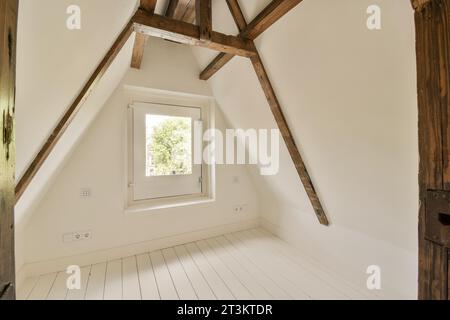 une chambre de style grenier avec parquet blanc et poutres apparentes au plafond au-dessus est une fenêtre qui donne sur Banque D'Images