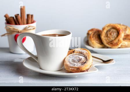 Petits pains à la cannelle sucrés et croustillants fraîchement cuits au four. Sur fond blanc, avec une tasse de café Banque D'Images