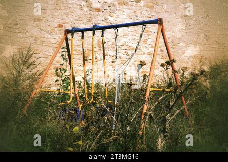 Balançoire abandonnée dans des chardons dans une image effrayante et grungy. Banque D'Images