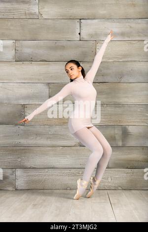 Corps entier jeune adolescente dans les chaussures de pointe exécutant la pose de ballet debout sur fond de bois Banque D'Images