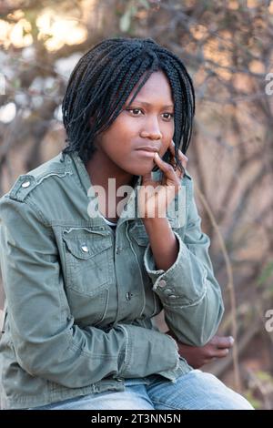 jeune femme africaine aux tresses , avec une expression pensive sur le visage, portrait en plein air dans le village Banque D'Images