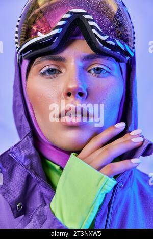 jeune femme en masque de ski, googles et veste chaude regardant loin sur fond violet, beauté de l'hiver Banque D'Images