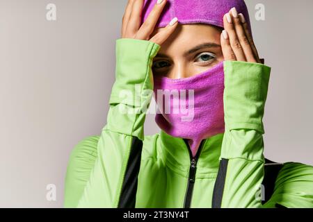 portrait de femme sportive avec les yeux bleus portant un masque de ski violet et regardant la caméra sur gris Banque D'Images