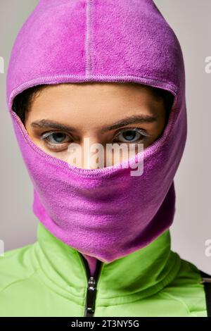 portrait de jeune femme avec les yeux bleus dans le masque de ski violet regardant la caméra sur fond gris Banque D'Images