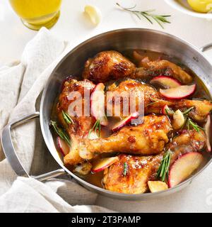 Vue rapprochée des pilons de poulet cuits avec des pommes et des herbes dans une casserole sur fond blanc. Banque D'Images