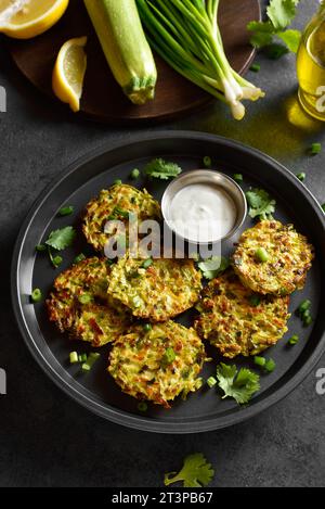 Vue rapprochée des beignets de courgettes de légumes avec oignon vert sur fond de pierre sombre. Banque D'Images