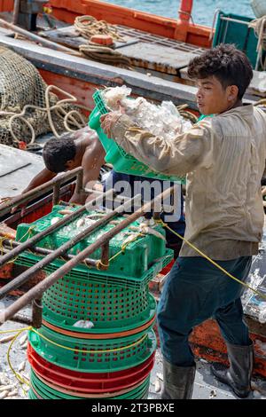 Village de pêcheurs de Samaesan, Thaïlande, 1 septembre 2023 : les ouvriers déchargent des vannettes de poisson d'un bateau de pêche et les empilent pour des acheteurs potentiels. Banque D'Images