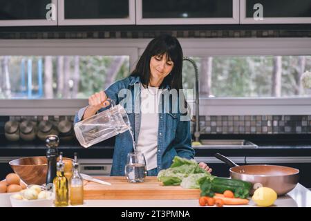 Femme versant de l'eau dans sa cuisine. Banque D'Images