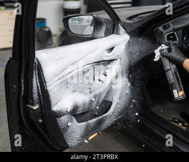 Un homme pulvérise de la mousse nettoyante sur l'intérieur d'une voiture. Banque D'Images