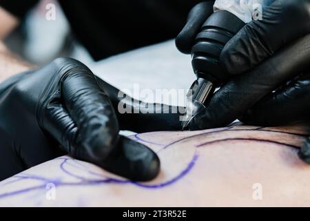 Tatoueur professionnel fait un tatouage sur la jambe masculine, gros plan. Homme faisant tatouage dans le salon. Banque D'Images