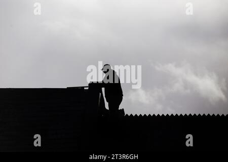 silhouette noire de constructeur (couvreur) sur le toit d'une maison contre un ciel nuageux gris Banque D'Images