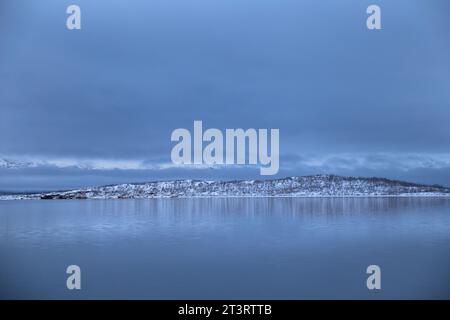 Vue panoramique sur le lac Torneträsk avec montagne enneigée sous un ciel nuageux sombre en hiver dans le parc national d'Abisko Banque D'Images
