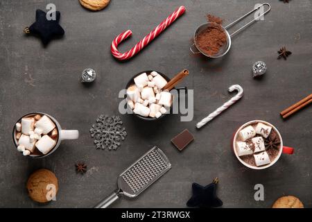 Tasses de cacao de Noël savoureux avec guimauves, biscuits, cannes de bonbons, boules, flocon de neige, chocolat, grille et cannelle sur fond noir Banque D'Images