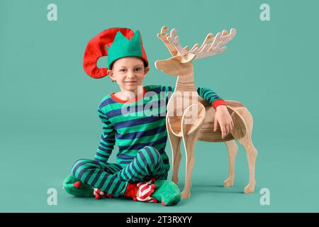 Mignon petit garçon en costume d'elfe avec renne en bois sur fond vert Banque D'Images