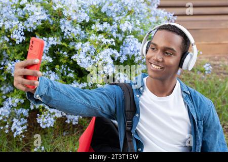 Jeune homme afro-américain prenant un selfie avec un téléphone portable et souriant à l'extérieur. Banque D'Images