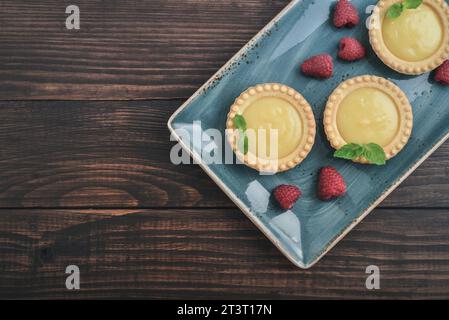 Mini-tartes avec remplissage de citron, framboise et crème anglaise sur planche rustique en bois vue de dessus Banque D'Images