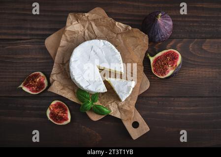 Camembert avec figues fraîches et basilic servi sur planche à découper sur fond de bois foncé, vue de dessus Banque D'Images